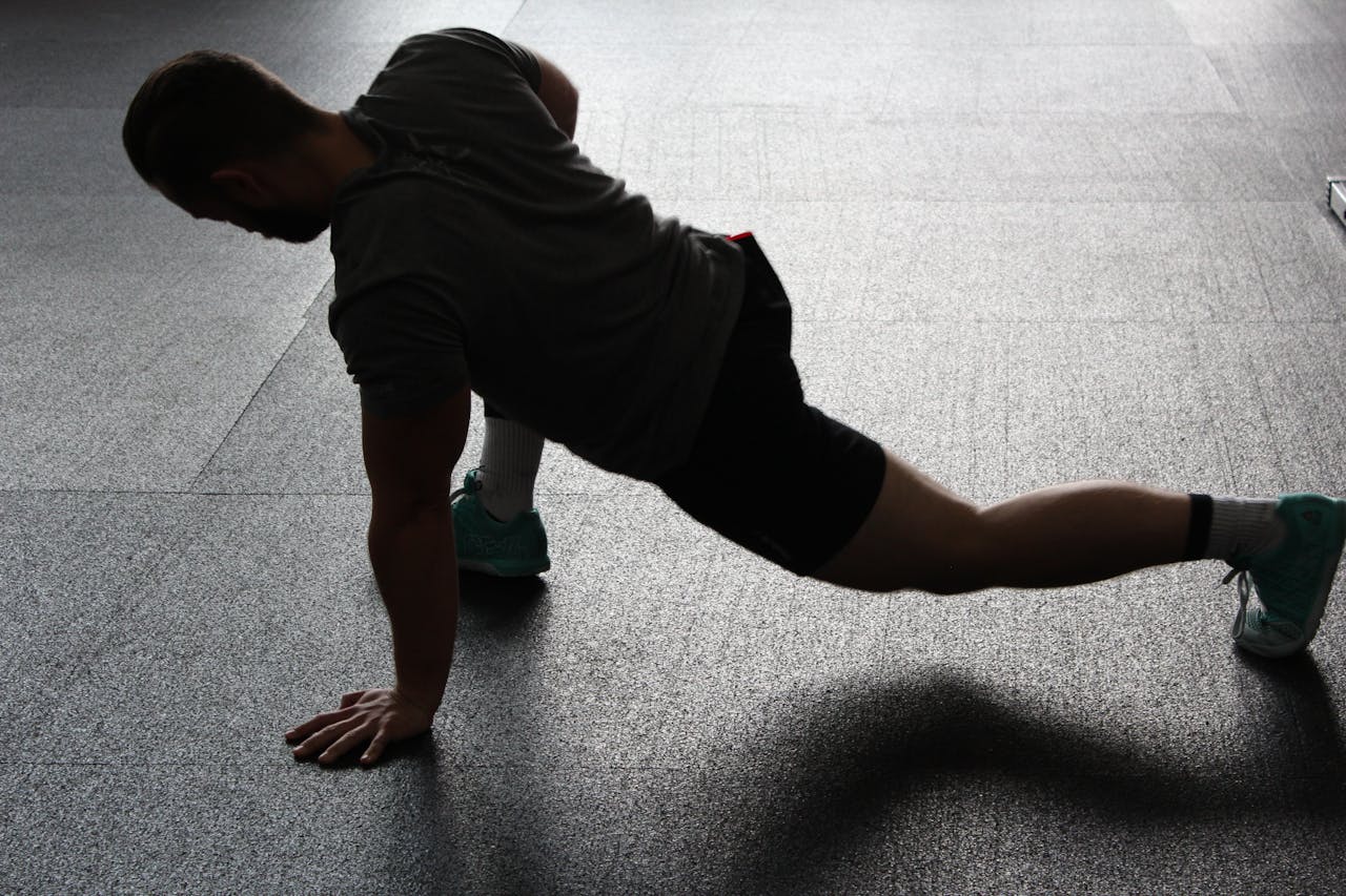 Silhouette of a man executing a stretching routine in a dim gym environment.