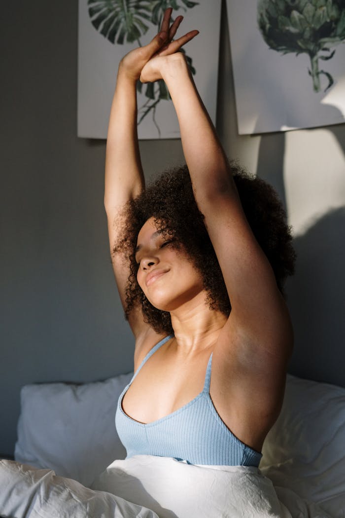 Woman with curly hair stretches joyfully in a sunny bedroom, embracing a peaceful morning.